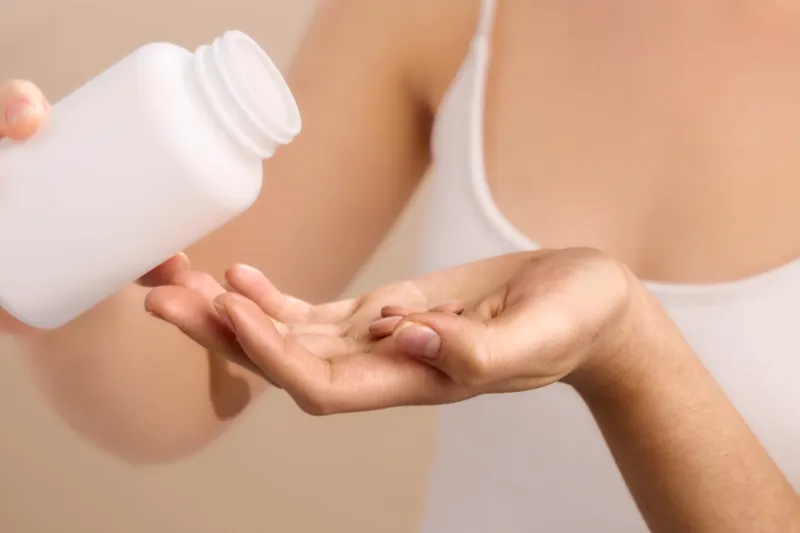Asian woman applies lotion on her hand in a clean studio setting, showcasing a gentle skincare routine. The scene conveys calm, moisture, and a modern personal wellness atmosphere.