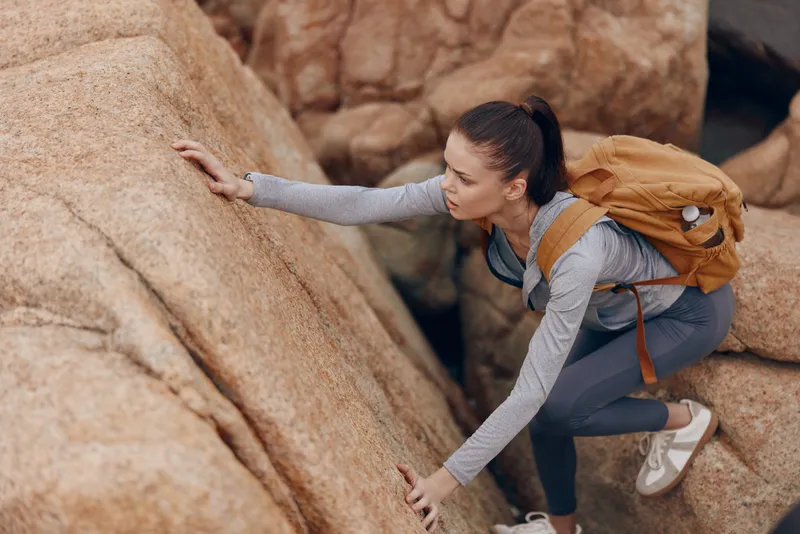 Female hiker scaling rocky terrain, demonstrating determination and adventure spirit in outdoor exploration during daytime