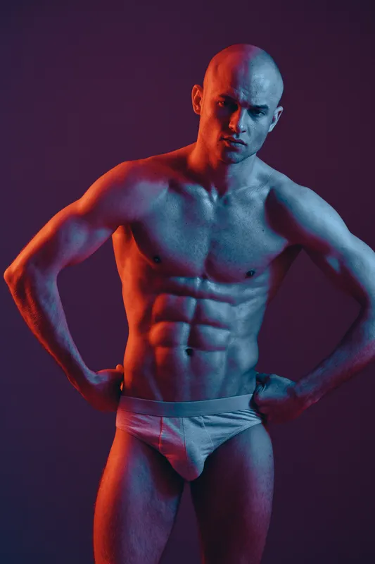 Muscular man posing in dramatic lighting emphasizes strength and fitness, showcasing a powerful silhouette against a vivid backdrop.