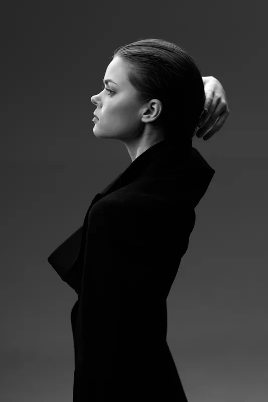 Black and white profile of a thoughtful woman wearing a dark coat against a grey background.