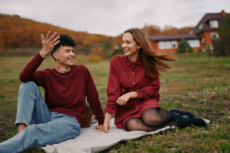 Two friends share a candid moment on a blanket in an autumn field, radiating authenticity and genuine connection under soft natural light and a relaxed, approachable mood.