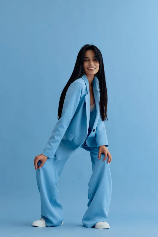 Young woman in blue suit posing confidently against plain blue background, showcasing modern style and professional attitude in studio setting.