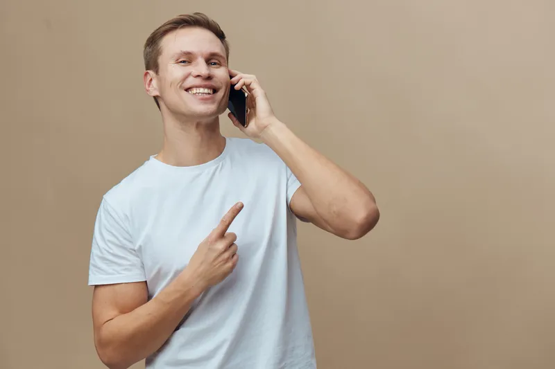 Smiling young man talking smartphone hand casual white t-shirt isolated beige background cheerful communication digital nomad concept