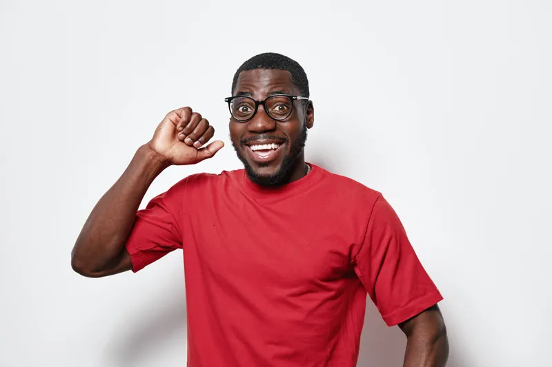 African American man with dark skin wearing glasses and red t shirt smiling and showing fist pump gesture isolated on white background for success and happiness concept.