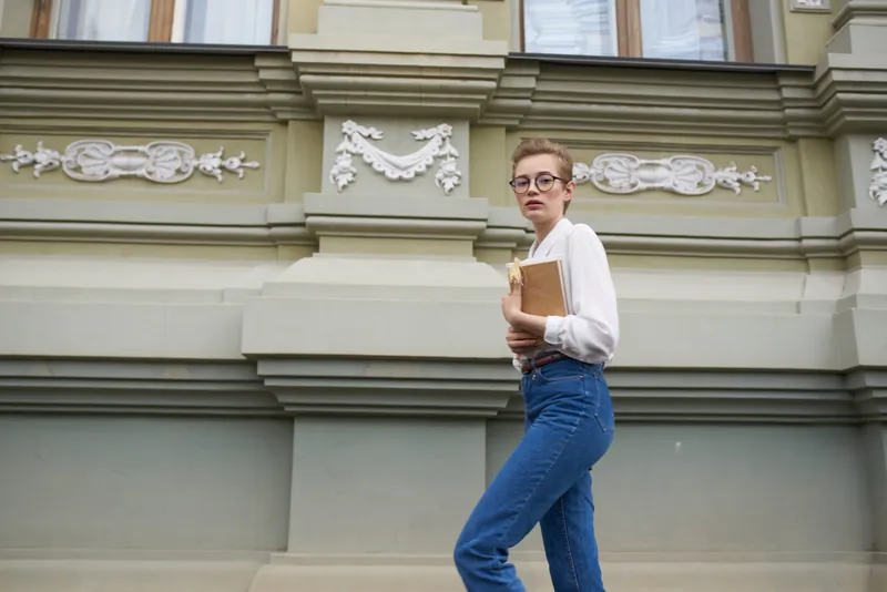 Привлекательная женщина в очках прогуливается по городу с книгой в руках
