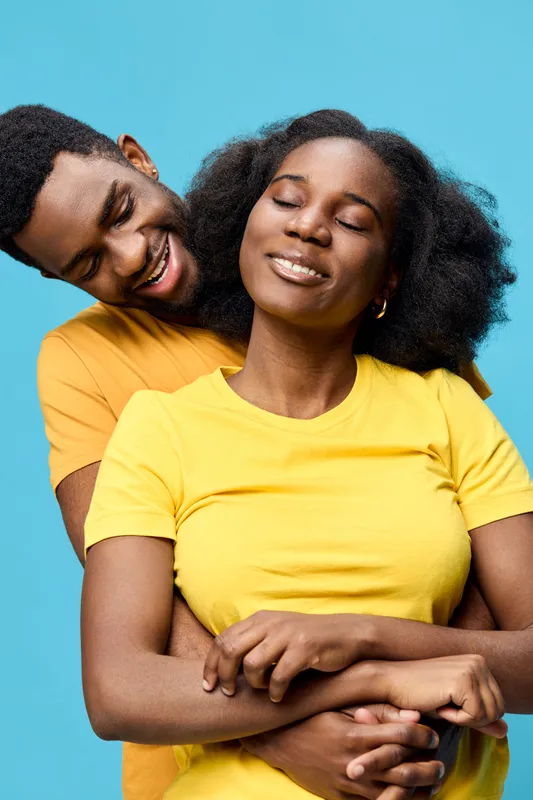 Joyful couple embracing with bright yellow shirts against a vibrant blue background, symbolizing love, happiness, and connection in a cheerful, warm atmosphere