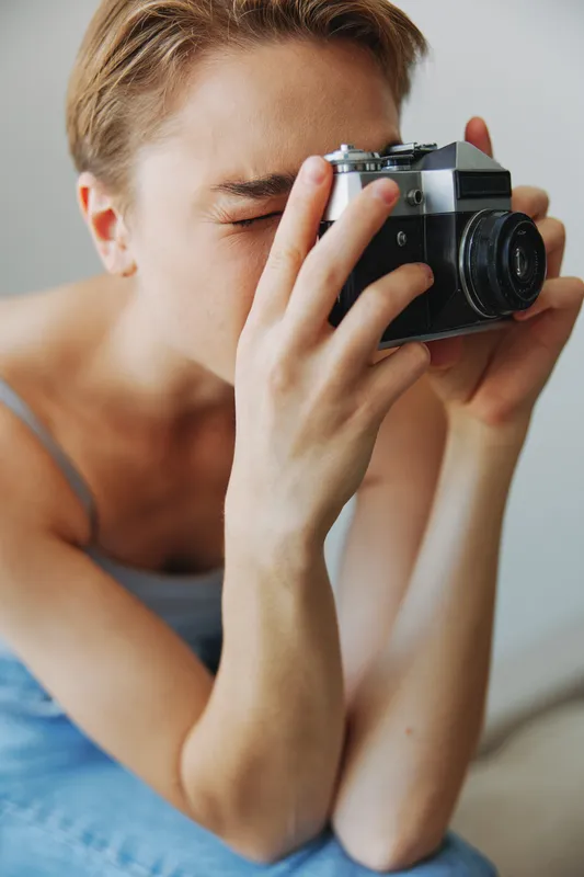 Женщина-фотограф снимает в студии на старую плёночную камеру, сидя дома на диване, портрет на белом фоне, есть свободное место для копирайтинга, внештатный фотограф