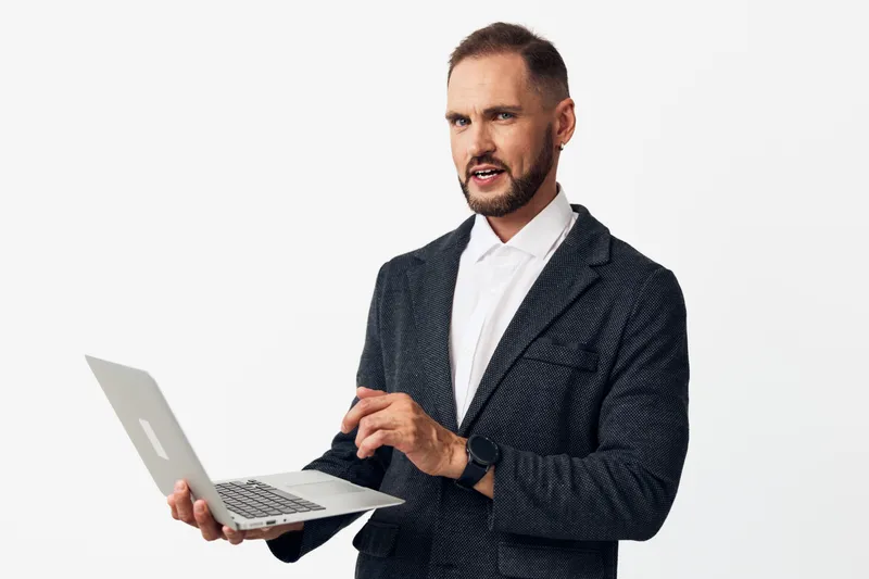 A professional man in a textured blazer uses a laptop on an isolated colored background, projecting focus and confidence while presenting ideas and solving tasks.