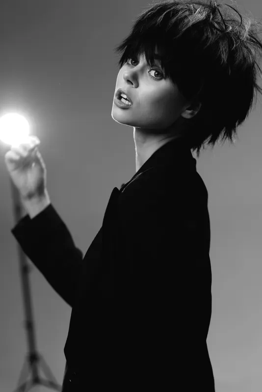 Black and white portrait of a young woman with short hair holding a bright light, stylish mood, monochrome aesthetic.