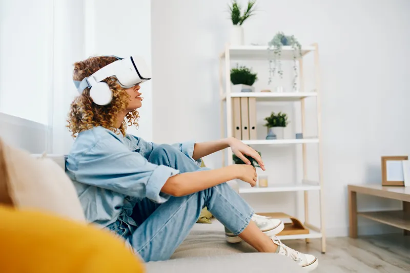 Улыбающаяся женщина наслаждается игрой в виртуальной реальности в VR-очках дома, в футуристической гостиной
