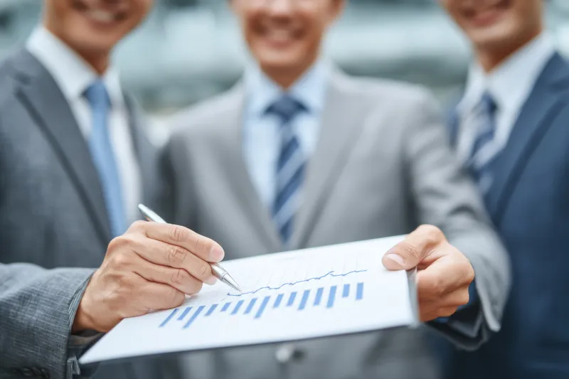 В светлом офисе коллеги совместно работают с данными и графиками, излучая уверенность, динамику и рост, когда завершают планы и стремятся к общим целям