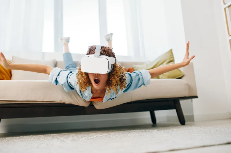 Улыбающаяся женщина в современных VR-очках в гостиной, радость от виртуальной реальности