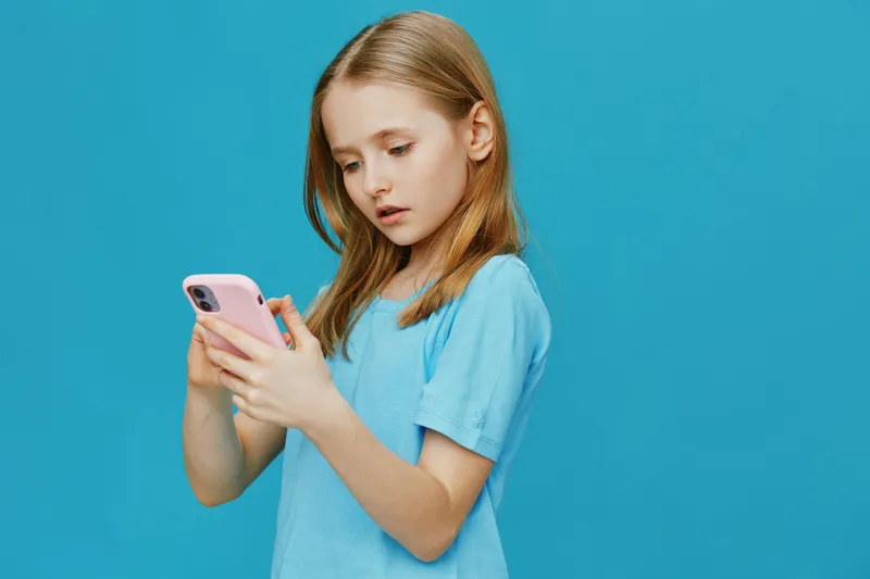 Young girl with straight hair using smartphone, wearing a blue t shirt against a solid turquoise background, showcasing curiosity and engagement