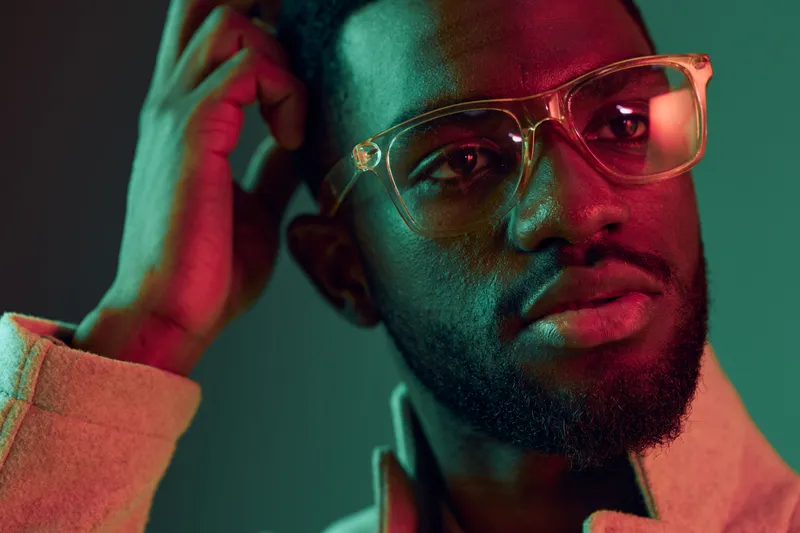 Stylish young Black man with glasses, expressing confidence in a colorful studio background, ideal for fashion, lifestyle, and emotion themed projects