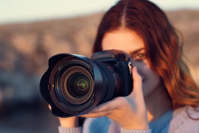 Симпатичная женщина с фотоаппаратом на природе в горах, на заднем плане река