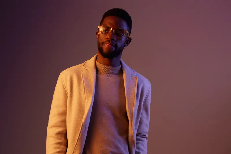 Confident African man in stylish outfit and glasses, against a vibrant purple background, embodying modern fashion and sophistication