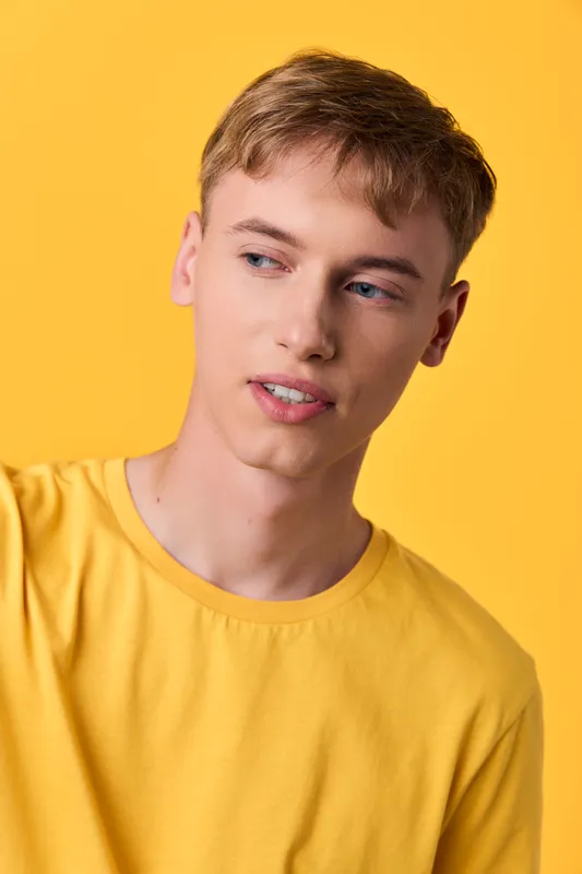 Man in a bright yellow t-shirt against a solid yellow backdrop, relaxed pose and subtle smile, studio photography conveying casual fashion and sunny mood for lifestyle or product shoots