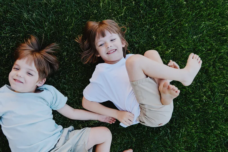 Two happy children playing on green grass, enjoying their childhood moments under the sun. They wear casual clothing and have joyful expressions.
