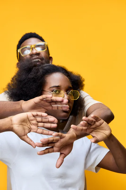 Young diverse couple expressing creativity and connection against a vibrant yellow background, showcasing emotions of joy and playfulness through their poses