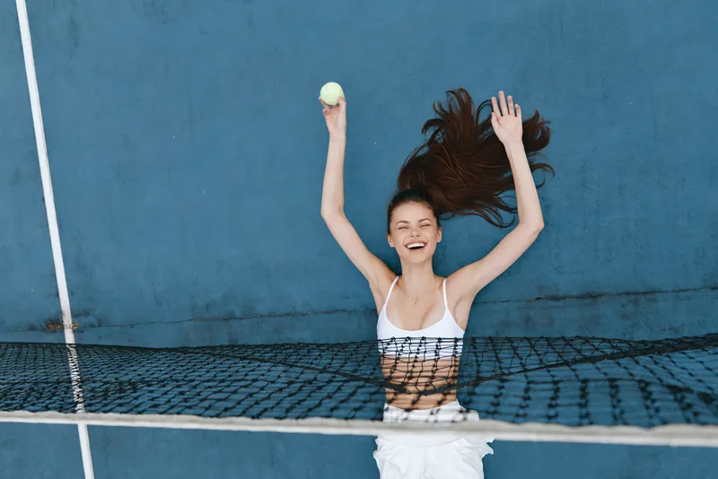 Joyful young female tennis player celebrating on the court, wearing a sporty outfit, showcasing healthy lifestyle and excitement, lively blue background