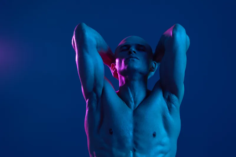 Athletic man posing under dramatic lighting, showcasing strength and confidence in a vibrant color atmosphere that evokes a sense of energy and dynamism.