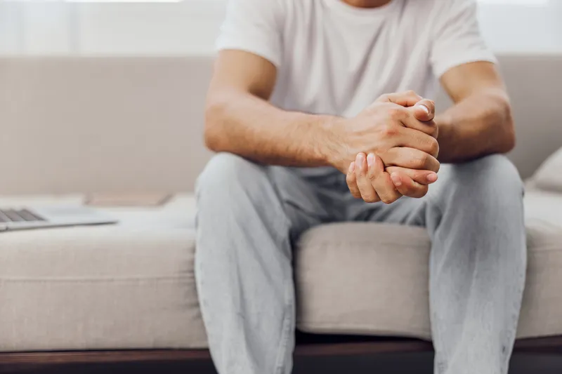 Pensive man sitting on a couch, reflecting on life. Casual attire, natural light creating a calming atmosphere. Perfect for modern lifestyle themes.