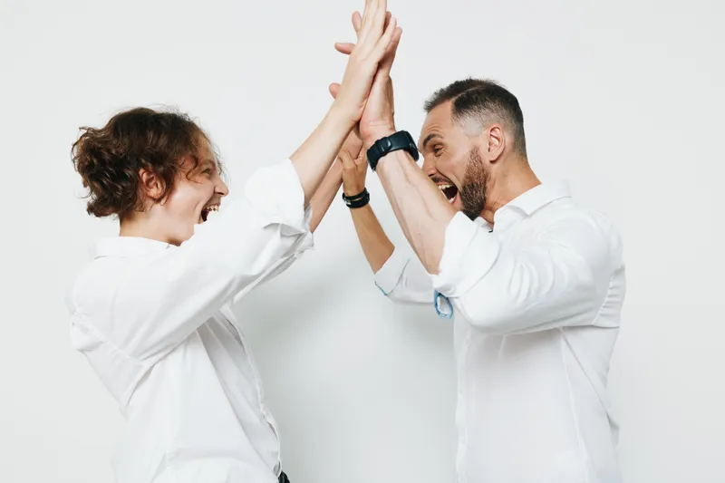 A professional man and colleague share a high five in a clean studio setting with a colored background, conveying strong emotion, victory, and teamwork in a confident business moment.