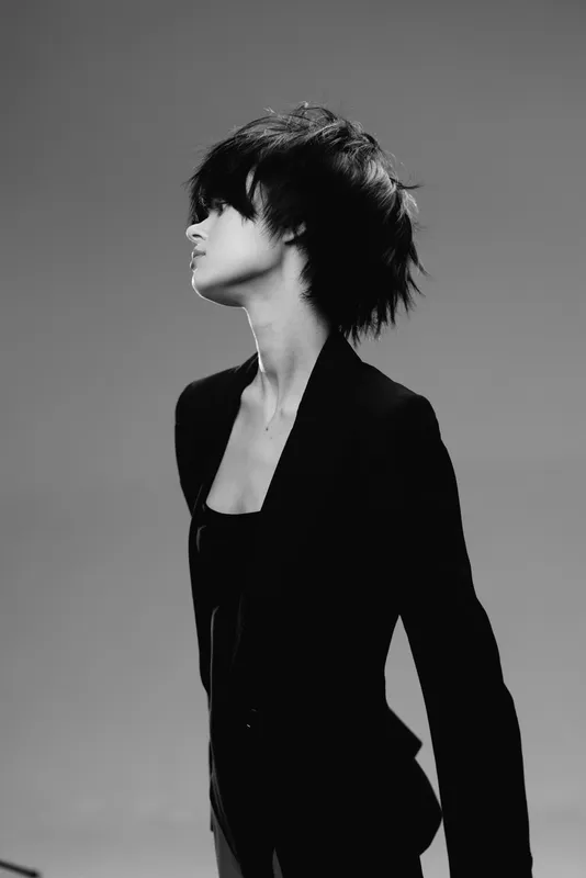 Black and white portrait of a young woman with short hair wearing a blazer, looking sideways with a serious expression.