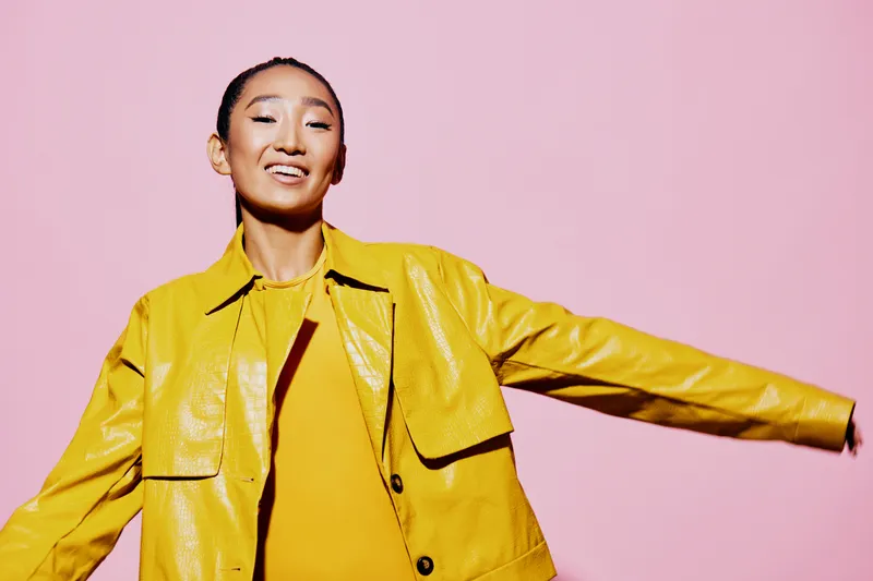 На студийном портрете молодая женщина с азиатской внешностью и каштановыми волосами выглядит удивлённой и счастливой