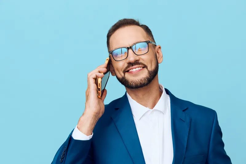 A confident male business professional on a vivid colored background, speaking on a phone, portraying focus, optimism, and polished style in a modern corporate portrait.
