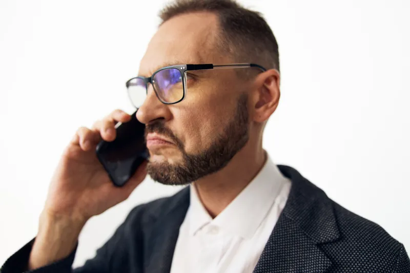 A professional male business portrait on a solid color background, captured during a phone call, showing a focused, determined expression and confident posture.