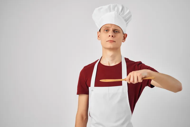 Повар-мужчина в белом фартуке, кухонная утварь, приготовление пищи в ресторане