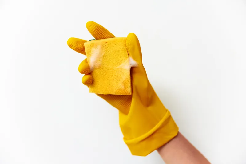 Человек в желтых резиновых перчатках держит губку с надписью «cleaning» на белом фоне