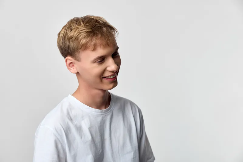 Smiling man in a white casual shirt stands in a neutral studio, creating a clean, friendly vibe ideal for lifestyle, marketing, or corporate content. Light, relaxed mood highlights approachable