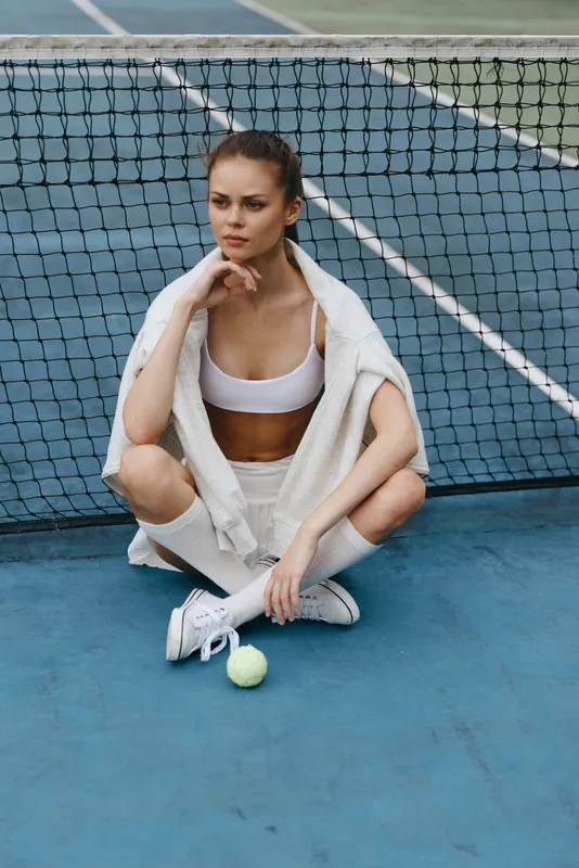 Young athletic woman in sportswear sitting on a tennis court, showcasing confidence and focus, ideal for promoting fitness and sports lifestyle photography
