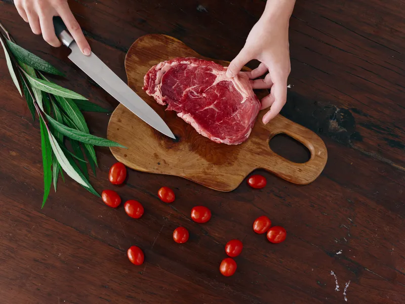 Женщина с ножом в руке нарезает свежее стейковое мясо для запекания на кухне