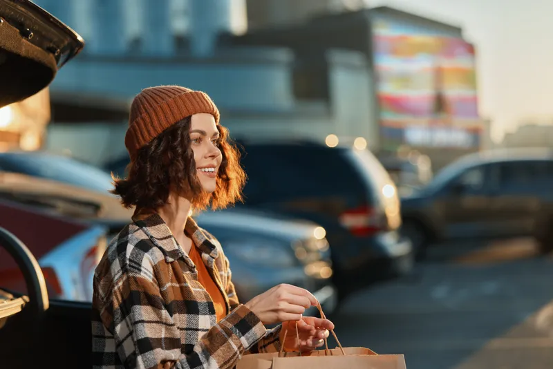 Woman shopping at a parking lot by car, smile and sunset light capture candid lifestyle and authenticity with golden hour glow, mindful living and emotional storytelling vibe.