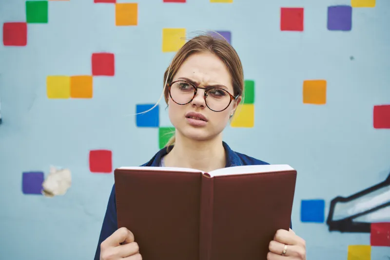 Удивленная студентка в очках на улице с книгой, эмоции, модель