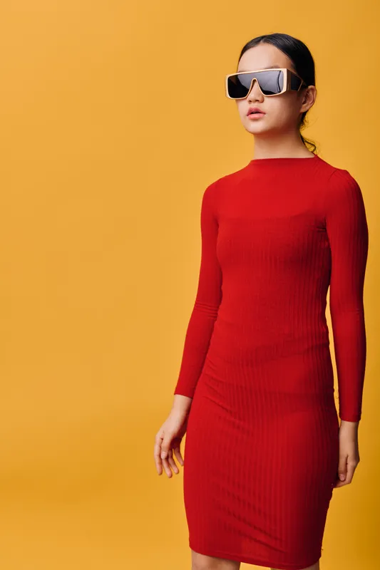 Woman standing in red dress and dark sunglasses against orange background. Fashion, portrait and style concept with confident female model and modern casual look for urban outfit.