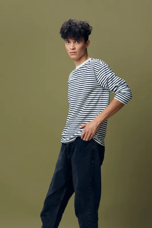 young man in striped shirt standing against olive background, casual style, curly hair, looking at camera with serious expression