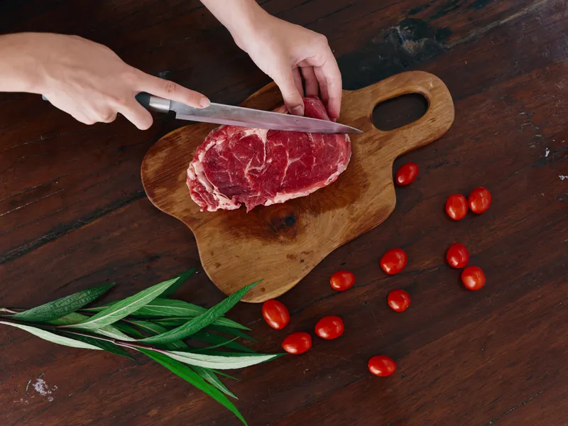 Женщина с ножом в руке нарезает свежее мясо стейка для жарки на кухне