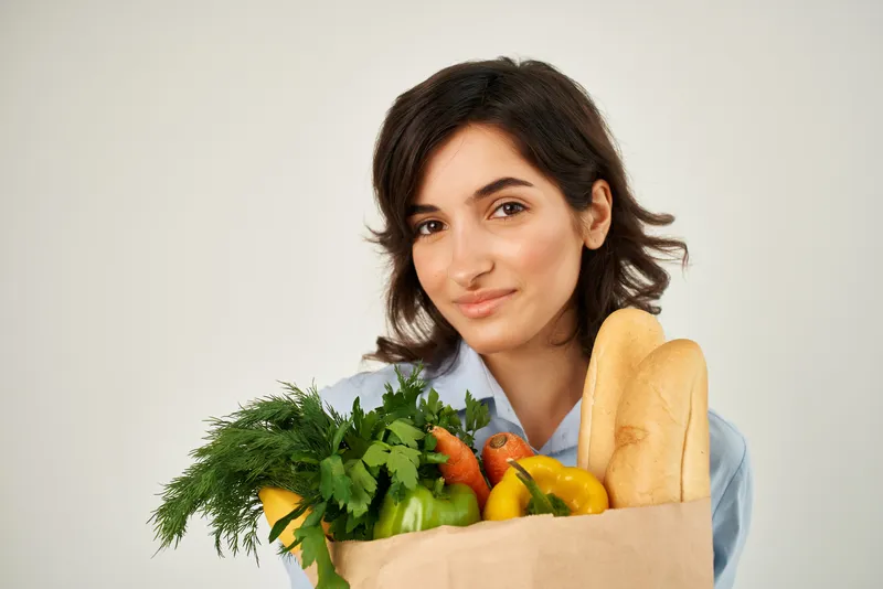 Женщина в синей рубашке упаковывает продукты в супермаркете, совершая покупки здоровой пищи