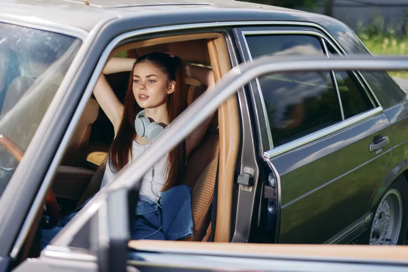 Young woman relaxing in a car with headphones, showcasing a casual summer vibe and a serene expression, perfect for lifestyle and travel themes.