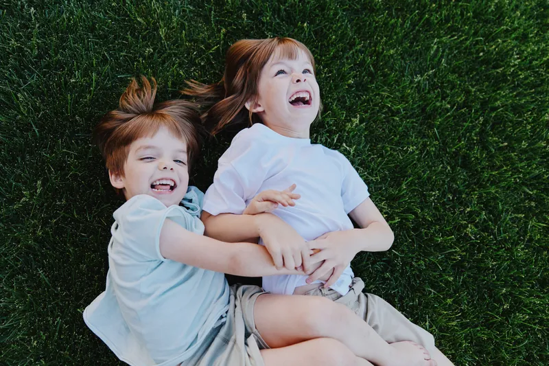Happy children enjoying playful moments outdoors, laughing and embracing on green grass, radiating joy and innocence in a vibrant setting.