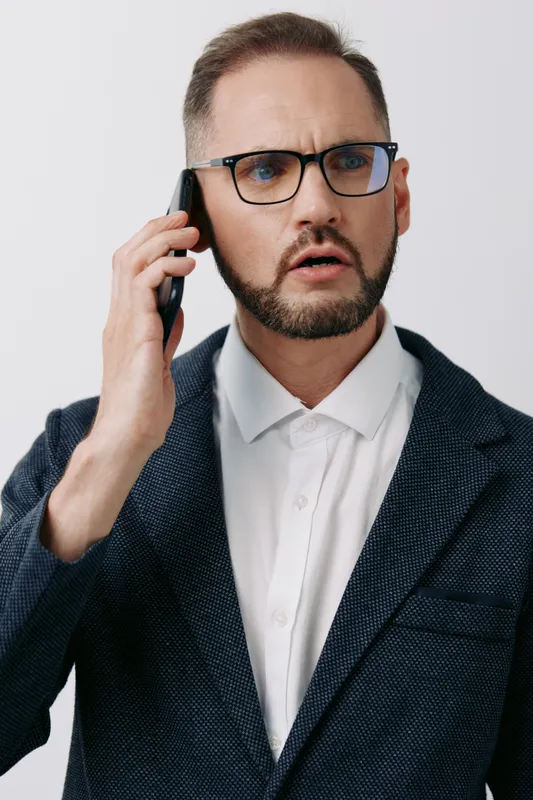 Professional man on a colorful solid background, talking on a mobile phone with a focused, concerned expression, conveying business communication and urgency in a modern work setting.