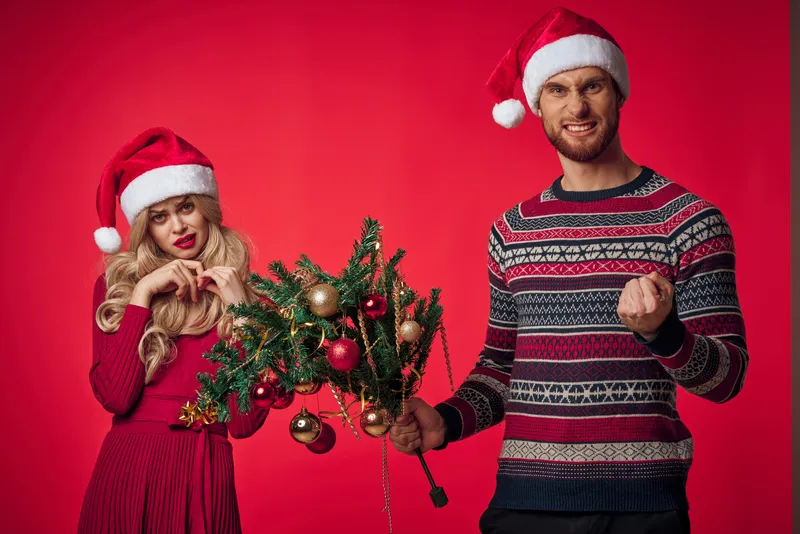 Весёлая молодая пара в рождественской одежде среди праздничных украшений и игрушек