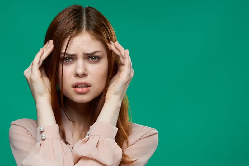Крупным планом женщина держится за голову, выражая недовольство и сильные эмоции на зелёном фоне