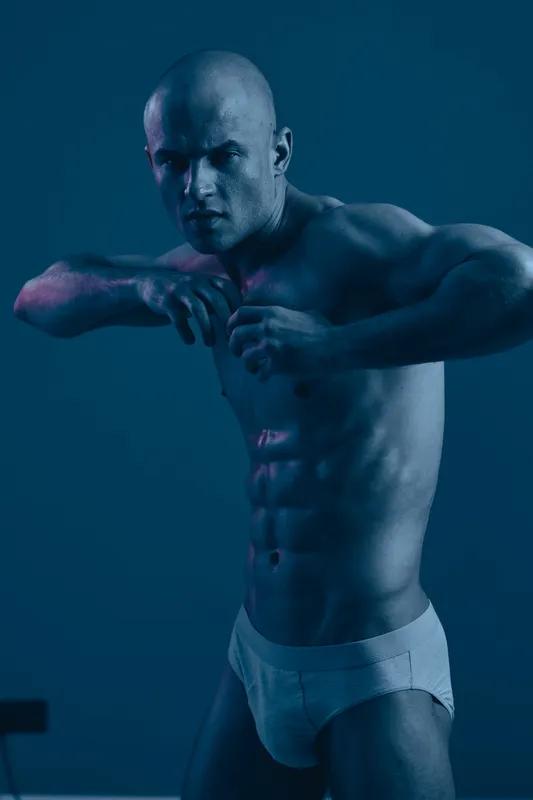Athletic man posing confidently in a dynamic posture, showcasing strength and determination. The image uses minimal color, emphasizing the subject's physique and intensity.