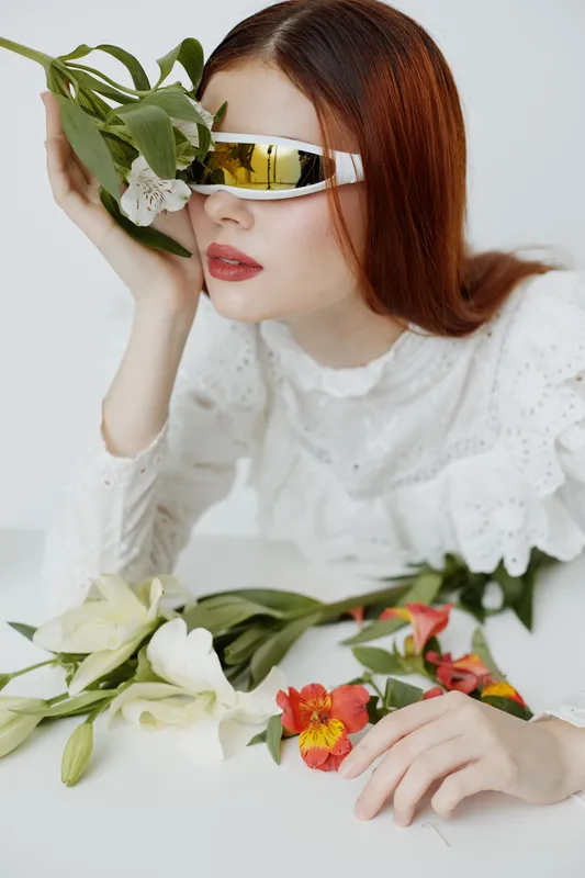Stylish woman with floral arrangement, wearing sunglasses, showcasing modern fashion, emotions of tranquility and elegance, bright colors against white backdrop