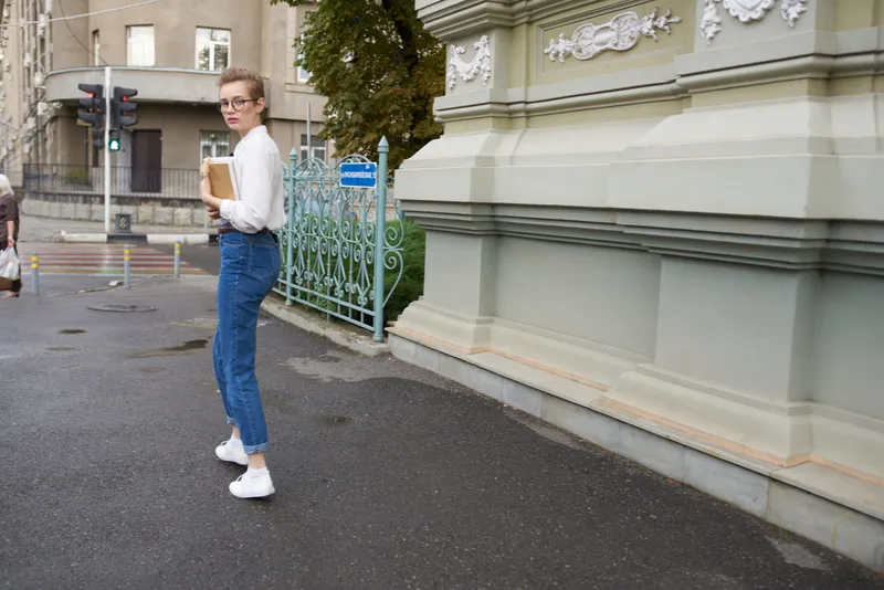 Женщина с короткой стрижкой и в очках прогуливается по городу с книгой, образование